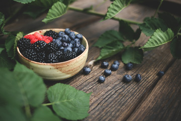 Bowl of freshly picked berries over wooden table and greenery