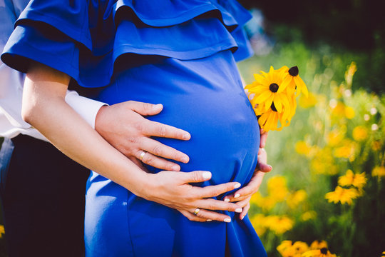 Father and pregnant mother holding hands together with yellow flowers on a green meadow.