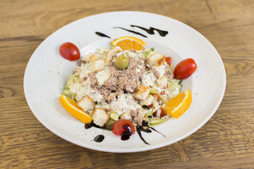 Tuna salad with lettuce, olives, and tomatoes. Orange decoration on a white plate. 