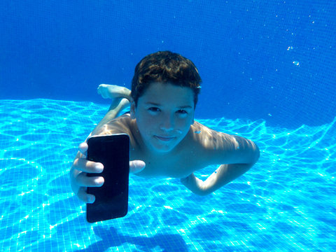 El ni&ntilde;o esta hablando por telefono movil abajo del agua en la piscina.