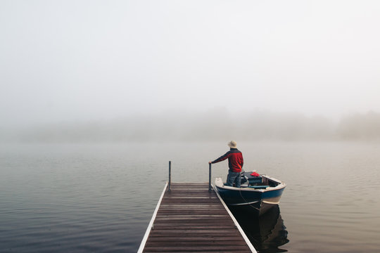 Man standing with boat near a dock on foggy lake.