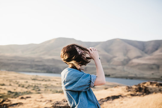 woman standing in windy field with mountains at sunset
