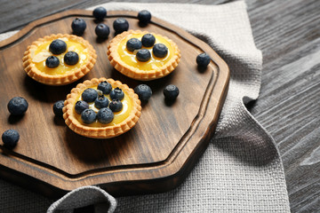 Delicious crispy tarts with blueberries and custard cream on wooden board