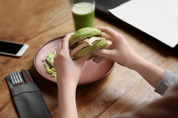 Woman eating tasty green sandwich over table