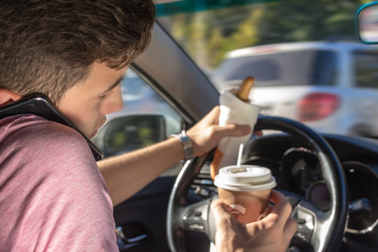 yang men driving car and eating coffee, talking on phone and holding a hot dog