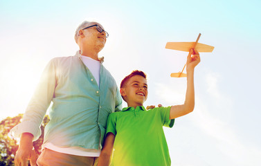 senior man and boy with toy airplane over sky