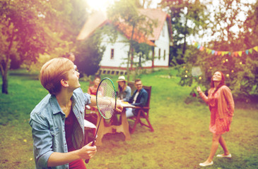 happy friends playing badminton at summer garden