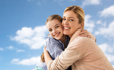 Obraz premium happy family of girl and mother hugging over sky