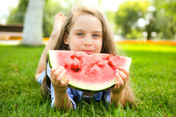Happy  adorable little girl laying on grass eating watermelon in summertime.Happy little girl  Having Fun outdoors in summer.