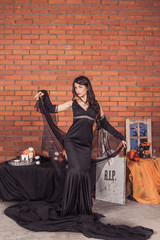 Naklejka premium sexy girl in costume of witch.Halloween decorations with spiders and pumpkin bucket for trick or treat. Greeting Card.Halloween pumpkin brick background.Happy Halloween postcard. Ideas for Halloween. 