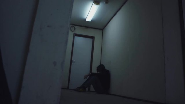 Silhouette of a depressed man sitting on the floor at dark stone corridor with flashing lamp. Young Man Struggling with Failure and Loneliness