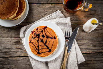 Ideas for breakfast are Halloween, food for children. Pumpkin pie pancakes decorated with chocolate syrup in a traditional style - spider web, spider, jack lantern. On wooden rustic table, copy space