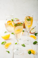 Drinks and cocktails. White autumn sangria with apples, orange, mint and white wine. In glasses for champagne, in a pitcher, on a white wooden table. Copy space
