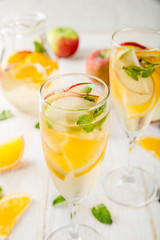 Drinks and cocktails. White autumn sangria with apples, orange, mint and white wine. In glasses for champagne, in a pitcher, on a white wooden table. Copy space