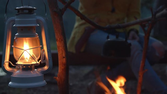 Old fashioned kerosene lamp lantern and female hiker drinking hot tea next to the fireplace