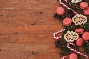 brown wooden background with branches of spruce, macaroons, and caramel sticks