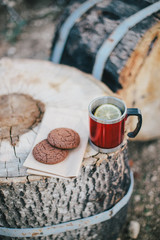 Red cup with tea and lemon and cookies on a wooden log in a forest