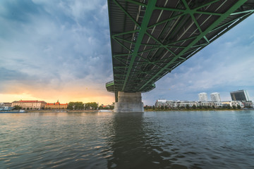 By the River under the Bridge. Skyline of Bratislava, Slovakia at Sunset in Background.