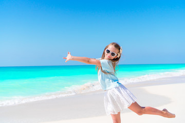 Fototapeta na wymiar Amazing little girl at beach having a lot of fun on summer vacation. Adorable kid jumping on the seashore