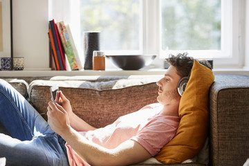 Young Man Using Tablet Computer And Headphones On Sofa