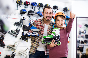 Male shop assistant helping boy to choose roller-skates in sports store