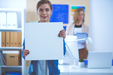 Two young woman standing near desk with instruments, plan and laptop.