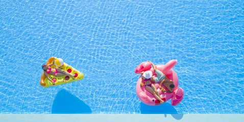 AERIAL, CLOSE UP: Beautiful couple and fit girl lying on fun colorful inflatable floaties, enjoying...