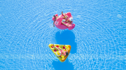 AERIAL CLOSE UP Beautiful couple and fit girl lying on fun colorful inflatable floaties, enjoying relaxing summer vacations in resort. Friends chilling, sipping drinks and sunbathing on floats in pool