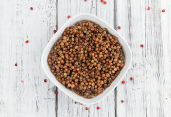Wooden table with preserved Pink Peppercorns, selective focus