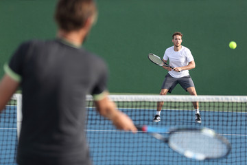 Men sport athletes players playing tennis match together. Two professional tennis players hitting ball on hard outdoor court during game. - Powered by Adobe