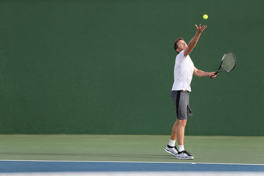 Tennis Serve Player Man Serving Ball During Match Point On Outdoor Green Court. Athlete Playing Sport Game Training Doing Exercise.