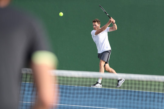 Tennis player man hitting backhand returning ball with racket on green background. Sports men playing together on outdoor court.