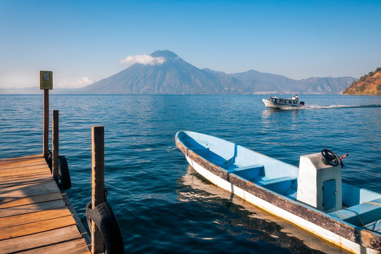 Beautiful View of Volcano San Pedro from the shore of Lake Atitlan in Guatemala with a tourist boat docked at a pier.
