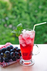  glasse of juice and  grapes on a wooden table outdoors