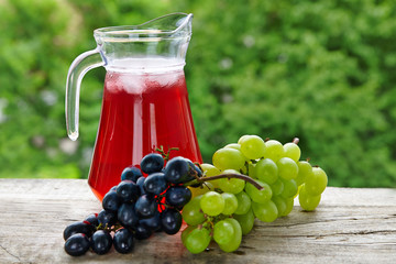 A jug of fruit juice with bunches of grapes on a natural background
