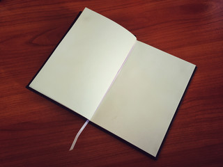 An open notebook on the wooden table. A blank notebook open on the table