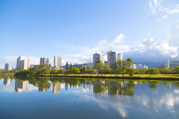The picturesque panorama of Waikiki suburbs framed by the mirror-like canal surface, green golf course and distant mountains. The view of Ala Wai Canal in Waikiki resort area, Honolulu, Hawaii.