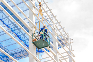 Worker man on a Scissor hydraulic Lift table Platform towards a factory roof at a construction site