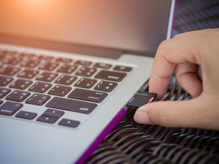 Closeup hand plugging memory card with laptop background.