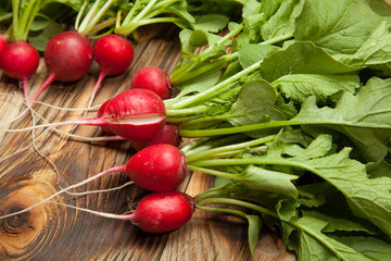 Red radishes in a wooden bowl on old table.