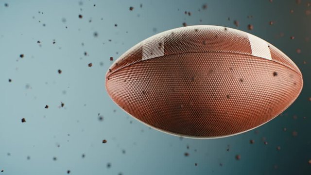 Computer animated sports background with leather football spinning and flying throw dust particles against blue background