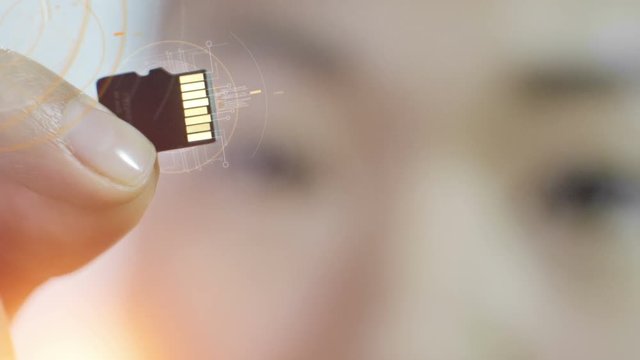 Closeup of Asian woman holding micro SD card with computer animated equalizers and data around it. Technological background