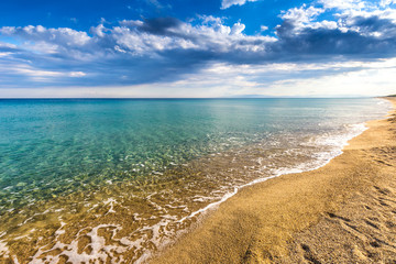 Sandy beach on the shore of the calm turquoise sea and clouds on blue sky in Italy, Europe.