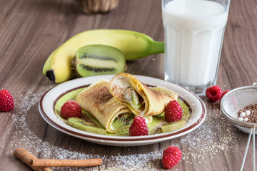 Homemade pancake with vanilla curd, raspberries, kiwi and banana pieces sprinkled with cocoa