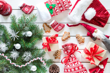 Christmas gifts, gift bag in christmas pattern, ginger cookies, toy felt Santa, red lamp  on wooden background, Christmas tree with decor, top view