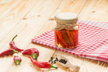preserved chili pepper  in glass jar on wooden table covered red squared napkin,  jars, pepper, wooden  scoop, copy space. free space for text