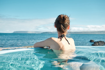Fototapeta na wymiar Young cheerful girl swimming in water of pool looking at the water on background of sea, Iceland, West Fjords. back view