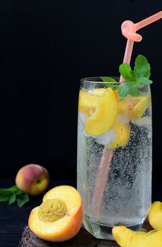 Glass of cold homemade peach lemonade or mojito cocktail with mint on dark background. Soda drink. Copy space. Photographing with natural light