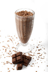 High caloric shake and frozen fast food drink concept with a glass of chocolate milkshake covered in shaved chocolate, some shavings got on the floor. Isolated on white background
