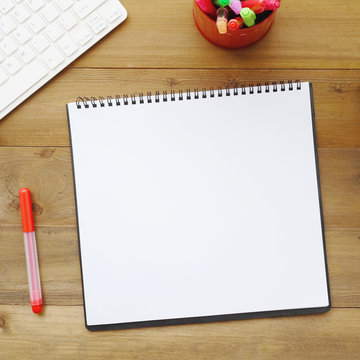Blank notebook paper, keyboard, mouse and pens on wood table background